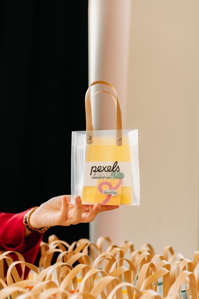 A person holding a transparent gift bag with Pexels branding, displayed elegantly by a hand.