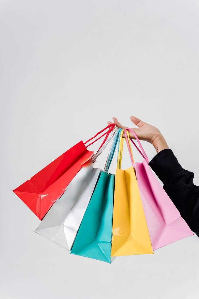 A hand holding colorful shopping bags against a white background, symbolizing retail and fashion.