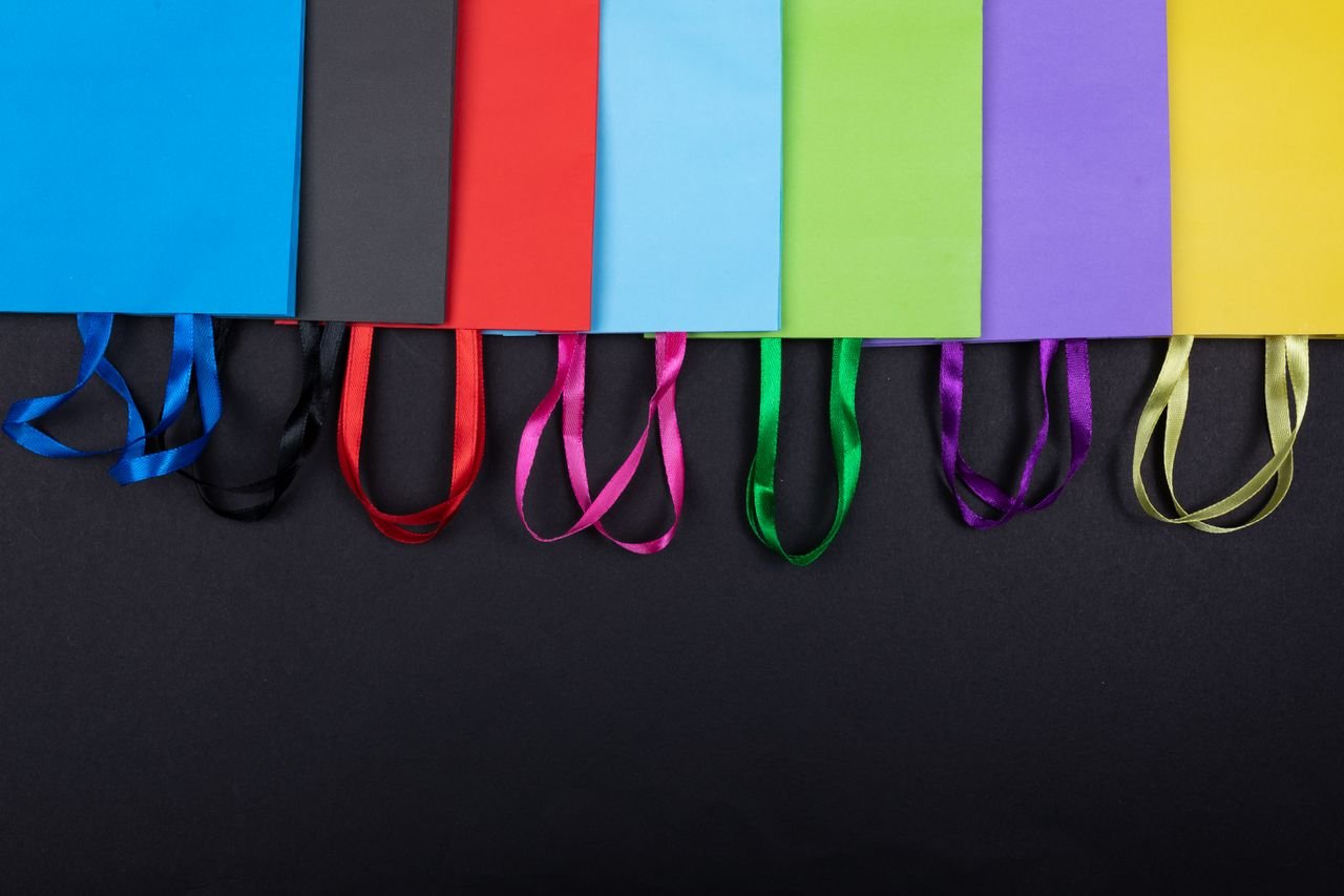 The Art of Drawing Readers In: Your attractive post title goes here Vibrant assortment of colorful shopping bags with ribbon handles on a black background.